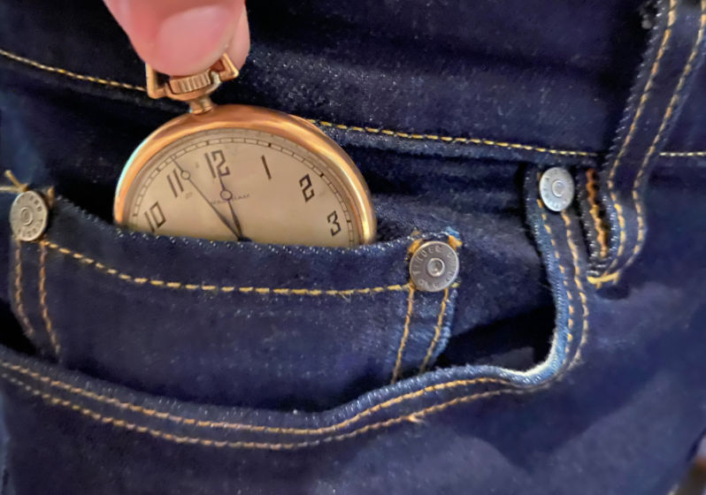 A guy putting stop watch in the little pocket of jeans.